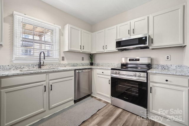 kitchen featuring a sink, wood finished floors, stainless steel appliances, white cabinets, and light stone countertops