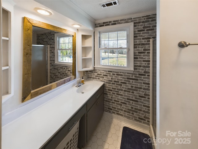 bathroom with a textured ceiling, vanity, a shower with door, and brick wall