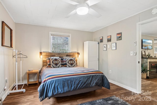 bedroom featuring crown molding, ceiling fan, a fireplace, and wood-type flooring