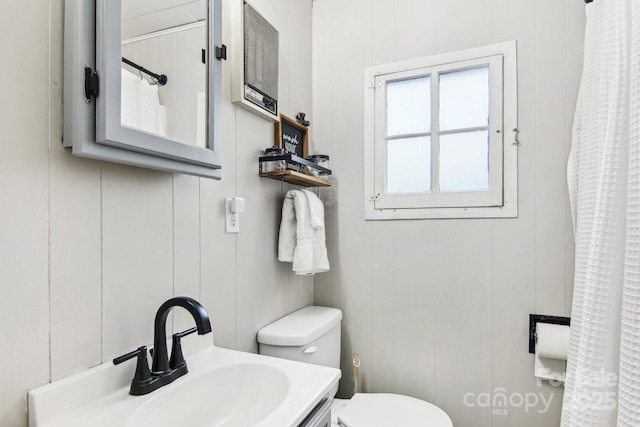 bathroom with vanity, wood walls, and toilet