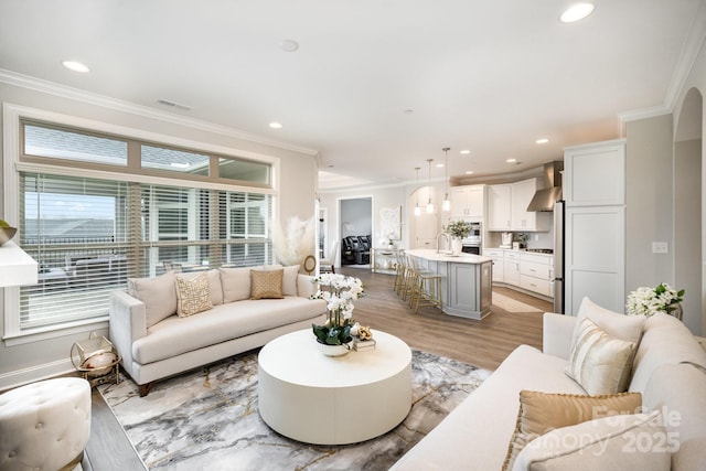 living room featuring ornamental molding, sink, and light hardwood / wood-style flooring