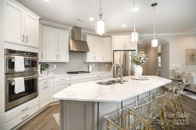 kitchen with appliances with stainless steel finishes, sink, a center island with sink, and wall chimney range hood