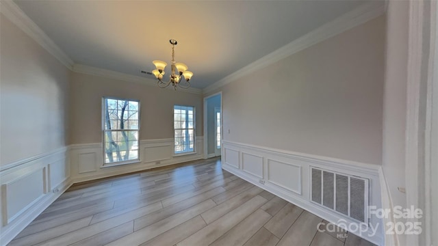 empty room featuring light hardwood / wood-style flooring, an inviting chandelier, and ornamental molding