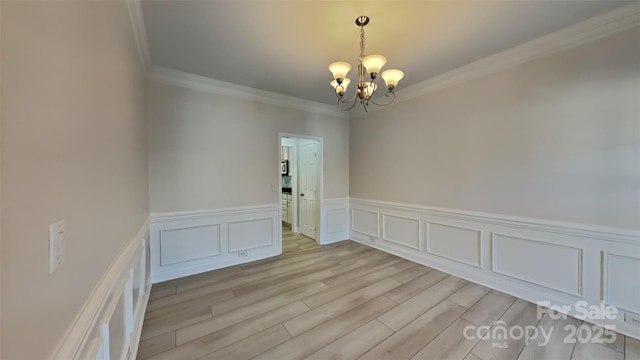 spare room featuring crown molding, light wood-type flooring, and an inviting chandelier