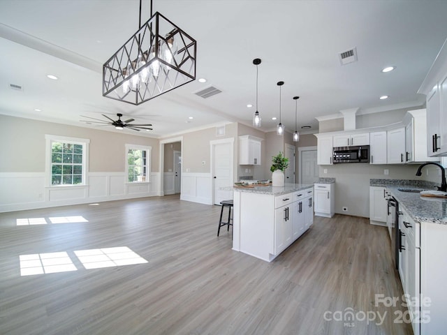 kitchen with white cabinetry, ceiling fan, hanging light fixtures, stainless steel appliances, and a kitchen island