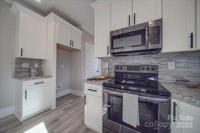 kitchen with stainless steel appliances, white cabinetry, and light stone counters