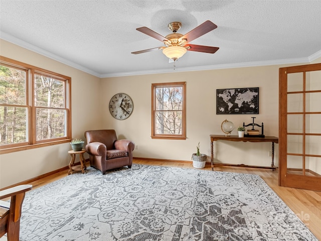 living area featuring ceiling fan, light hardwood / wood-style floors, ornamental molding, and a textured ceiling