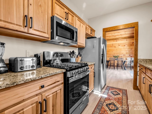 kitchen featuring wood walls, light wood-type flooring, light stone countertops, and stainless steel appliances