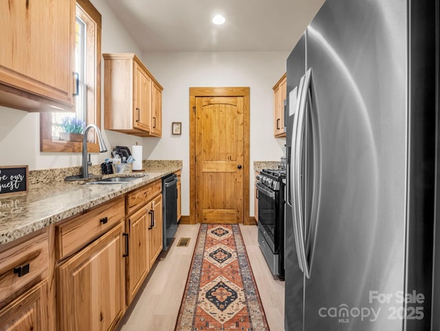 kitchen featuring light stone counters, sink, black appliances, light brown cabinets, and light hardwood / wood-style floors