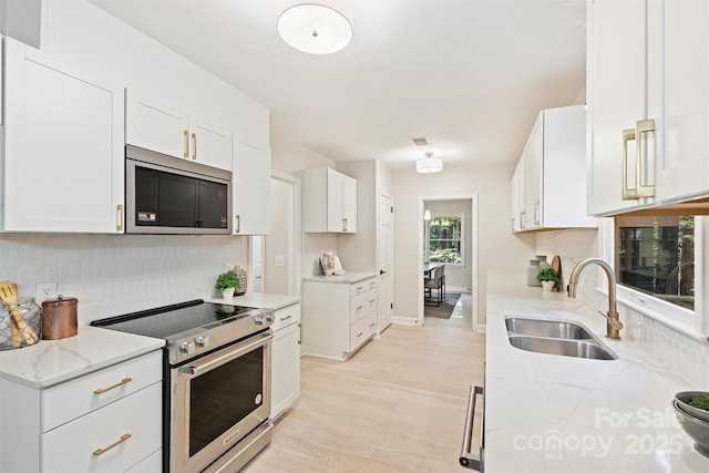 kitchen featuring light stone countertops, appliances with stainless steel finishes, decorative backsplash, sink, and white cabinetry