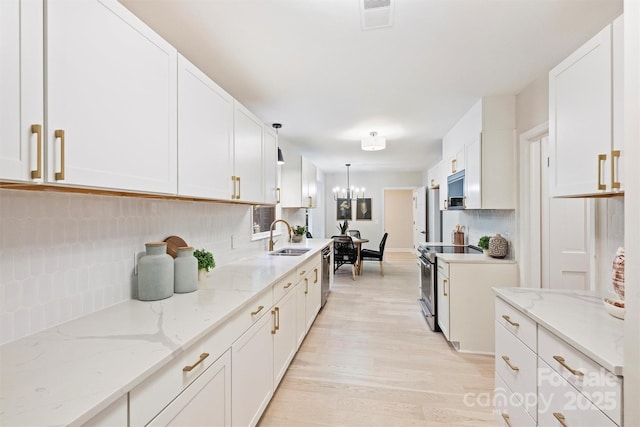 kitchen with pendant lighting, sink, appliances with stainless steel finishes, light stone counters, and white cabinetry