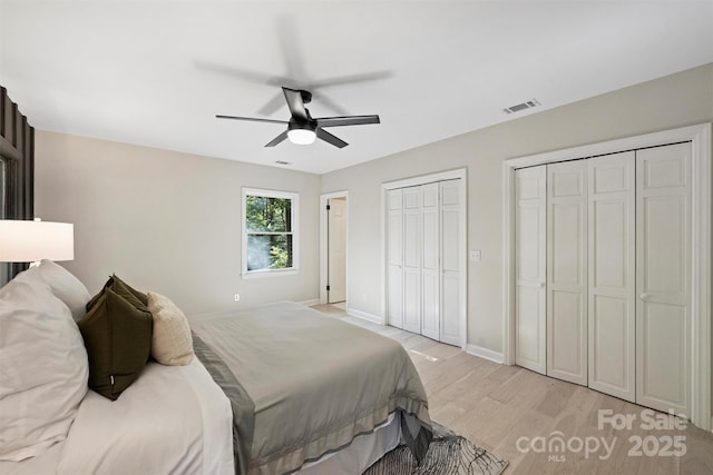 bedroom featuring ceiling fan, light hardwood / wood-style floors, and multiple closets