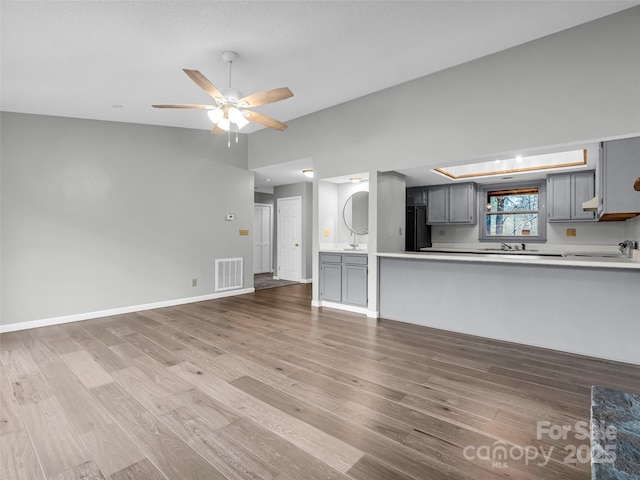 unfurnished living room featuring ceiling fan, sink, vaulted ceiling, and hardwood / wood-style flooring