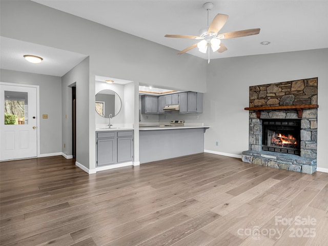 unfurnished living room with hardwood / wood-style floors, a stone fireplace, sink, vaulted ceiling, and ceiling fan