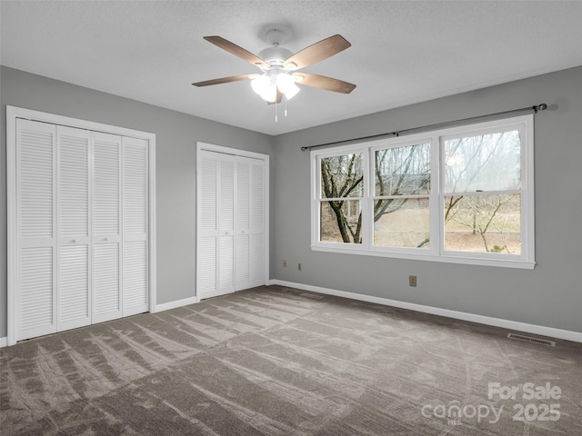 unfurnished bedroom with carpet flooring, ceiling fan, a textured ceiling, and multiple closets