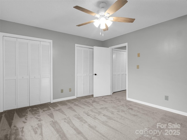 unfurnished bedroom featuring ceiling fan, light colored carpet, and two closets