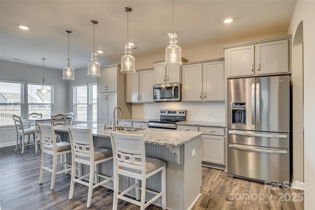 kitchen featuring sink, light stone countertops, stainless steel appliances, and hanging light fixtures