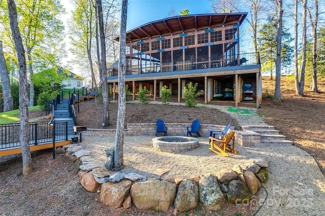 back of property with a sunroom, a deck, and an outdoor fire pit