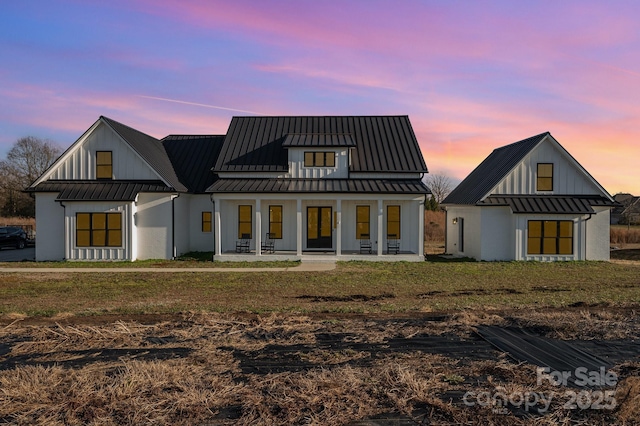 back house at dusk featuring a porch and a yard