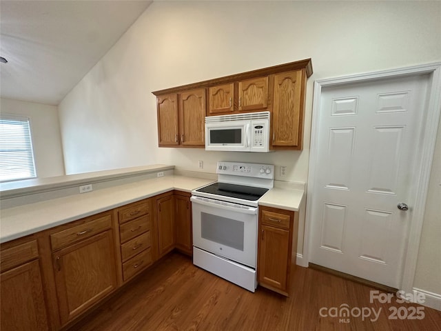 kitchen with lofted ceiling, kitchen peninsula, dark hardwood / wood-style floors, and white appliances