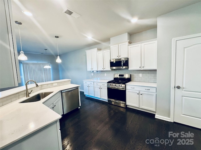 kitchen with sink, white cabinets, tasteful backsplash, pendant lighting, and appliances with stainless steel finishes