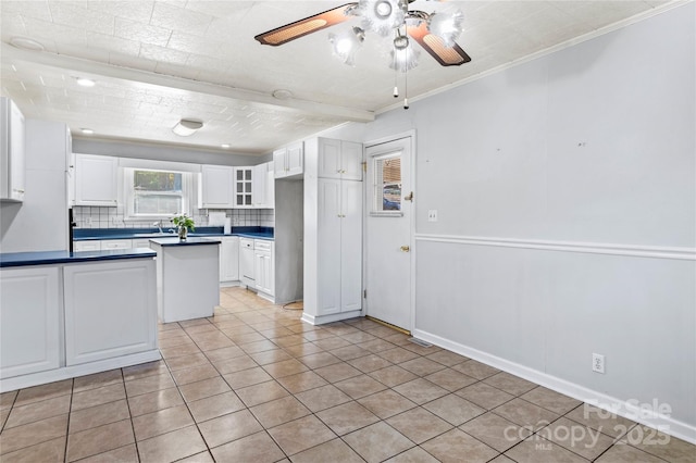 kitchen featuring sink, light tile patterned floors, backsplash, white cabinets, and ornamental molding