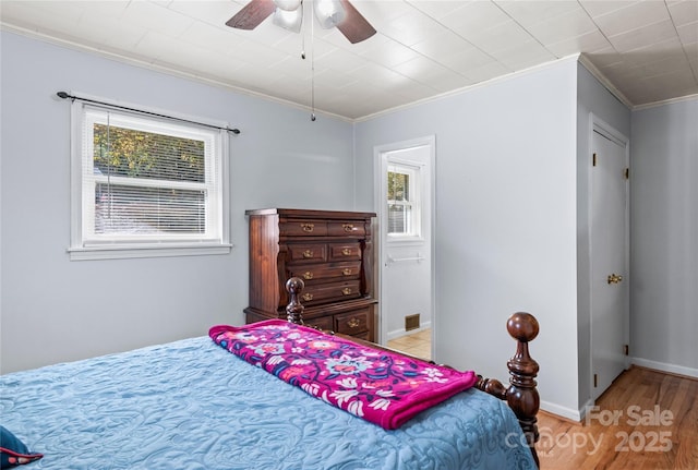 bedroom featuring multiple windows, light wood-type flooring, ceiling fan, and crown molding