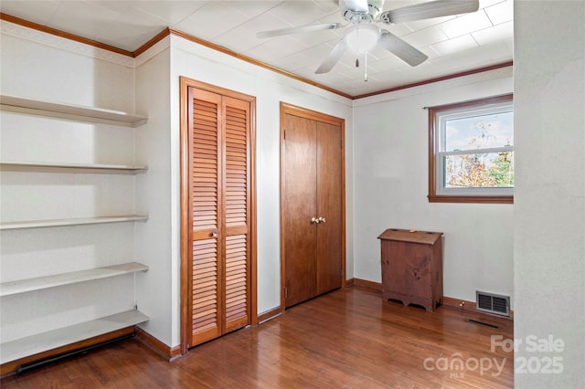 unfurnished bedroom with ornamental molding, ceiling fan, multiple closets, and wood-type flooring