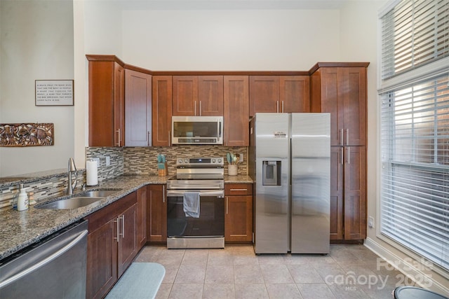 kitchen with sink, dark stone countertops, decorative backsplash, light tile patterned floors, and appliances with stainless steel finishes