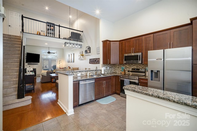 kitchen with a high ceiling, light tile patterned floors, light stone countertops, appliances with stainless steel finishes, and kitchen peninsula