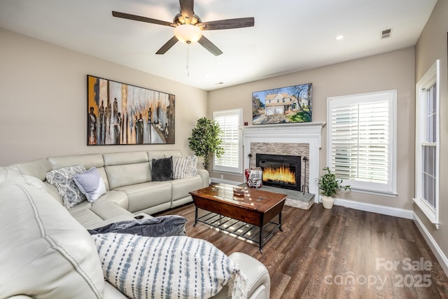 living room with dark hardwood / wood-style flooring, ceiling fan, and a stone fireplace