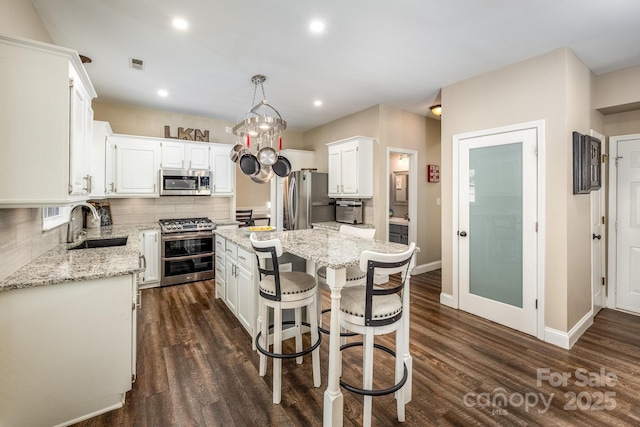 kitchen with pendant lighting, sink, appliances with stainless steel finishes, a kitchen island, and white cabinetry