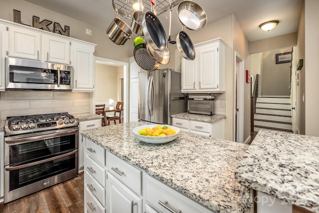 kitchen with light stone countertops, decorative backsplash, white cabinets, and stainless steel appliances