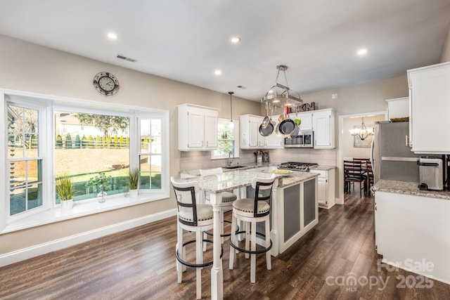 kitchen featuring white cabinets, light stone counters, stainless steel appliances, and hanging light fixtures