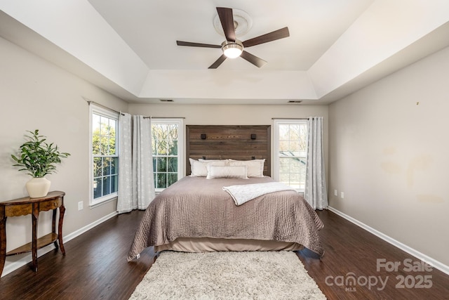 bedroom with ceiling fan, dark wood-type flooring, multiple windows, and a tray ceiling