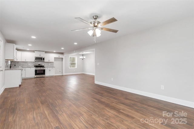 unfurnished living room featuring ceiling fan with notable chandelier and dark hardwood / wood-style floors