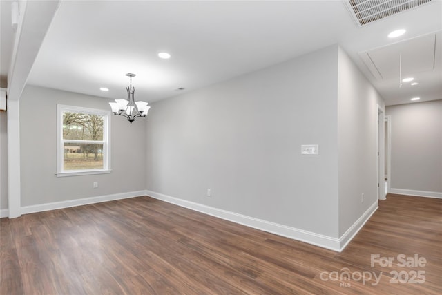 spare room featuring dark wood-type flooring and a chandelier