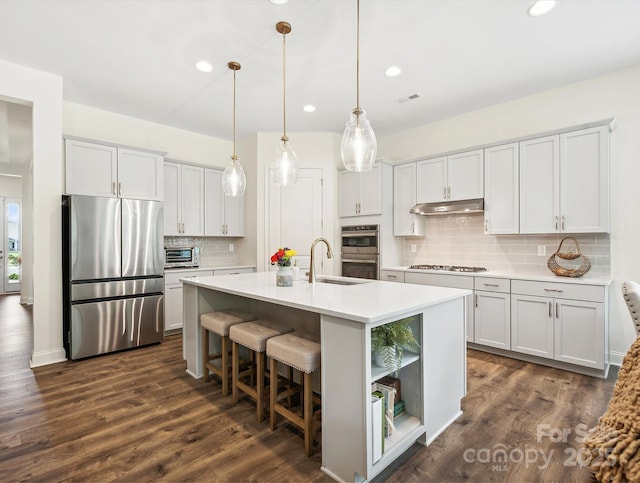 kitchen featuring sink, dark wood-type flooring, pendant lighting, a kitchen island with sink, and appliances with stainless steel finishes