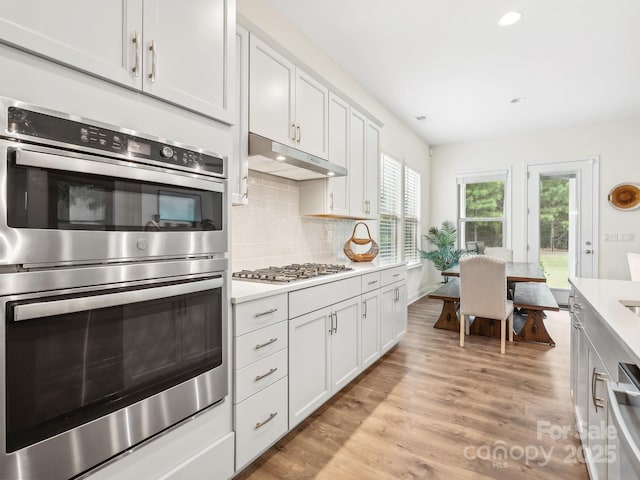 kitchen with decorative backsplash, white cabinetry, light hardwood / wood-style floors, and appliances with stainless steel finishes