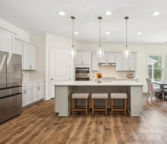 kitchen with white cabinetry, dark wood-type flooring, an island with sink, decorative light fixtures, and appliances with stainless steel finishes