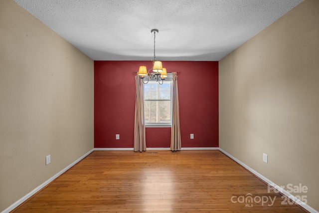 unfurnished room featuring wood-type flooring, a textured ceiling, and a notable chandelier