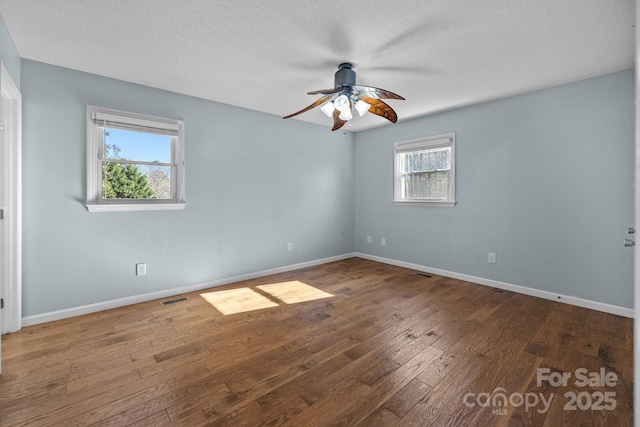 empty room with a textured ceiling, dark hardwood / wood-style flooring, and a wealth of natural light