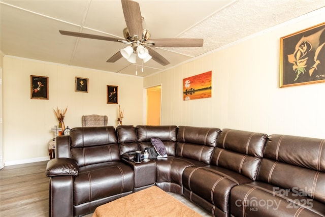 living area featuring baseboards, wood finished floors, ornamental molding, and a ceiling fan