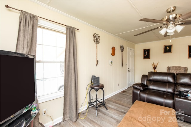 living area with crown molding, wood finished floors, baseboards, and ceiling fan