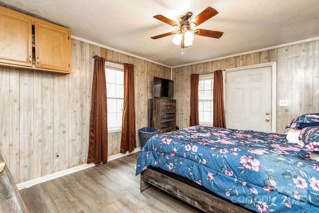 bedroom with a textured ceiling, wooden walls, crown molding, light wood finished floors, and baseboards