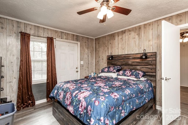 bedroom featuring ceiling fan, wood walls, ornamental molding, wood finished floors, and a textured ceiling