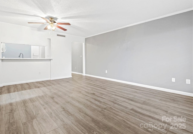 unfurnished living room featuring ceiling fan, ornamental molding, a textured ceiling, and light hardwood / wood-style flooring