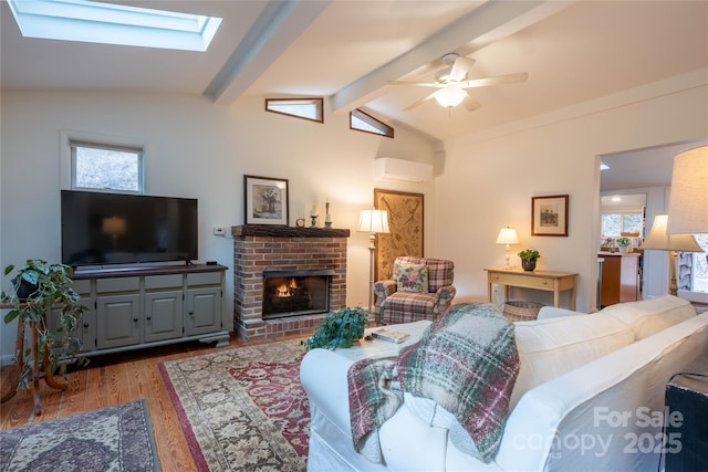 living room with hardwood / wood-style flooring, a fireplace, lofted ceiling with skylight, and ceiling fan