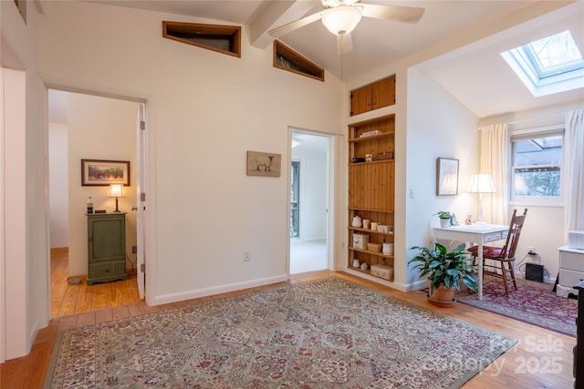 office area with lofted ceiling with skylight, built in shelves, ceiling fan, and light hardwood / wood-style flooring