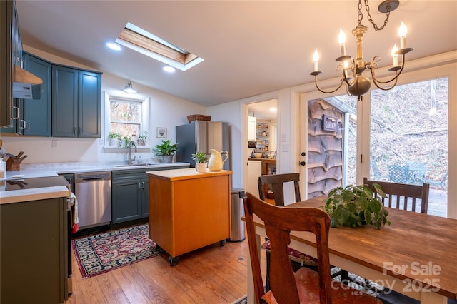 kitchen featuring sink, decorative light fixtures, light hardwood / wood-style flooring, stainless steel dishwasher, and vaulted ceiling with skylight